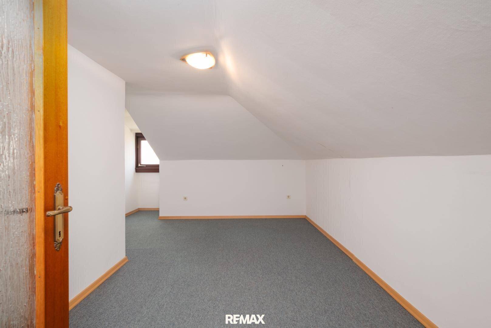 Geräumiges Dachzimmer mit Teppichboden und schrägen Wänden, ideal als Schlaf- oder Arbeitsbereich.