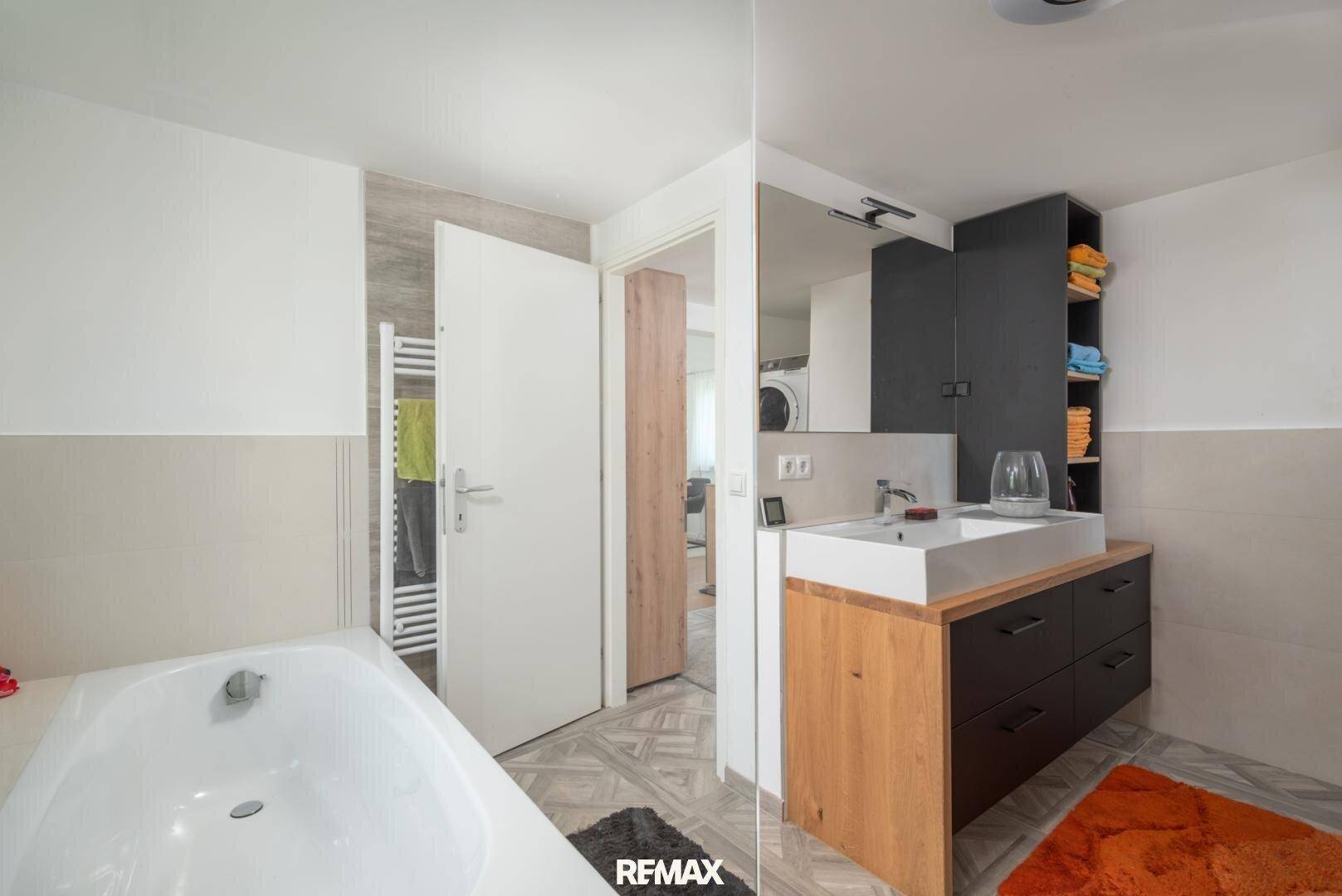 Modernes Badezimmer mit Badewanne, Einzelwaschbecken und dunklen Akzenten.