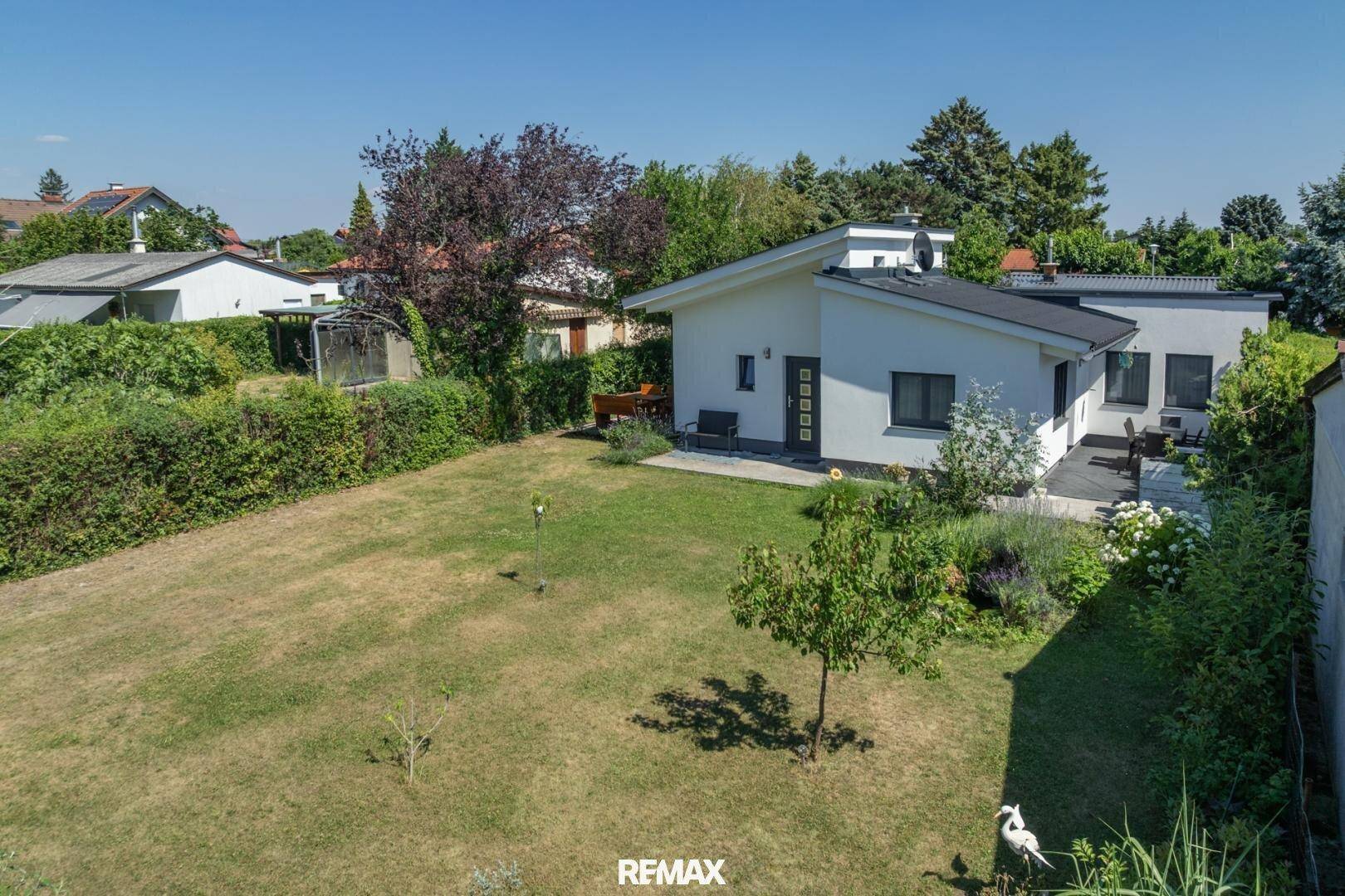 Weitläufiger Gartenbereich mit Rasenfläche und Einfamilienhaus unter blauem Himmel.