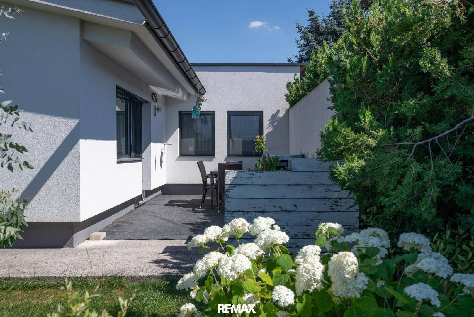 Gemütliche Terrasse am Haus mit Gartenmöbeln und blühenden Hortensien im Vordergrund.