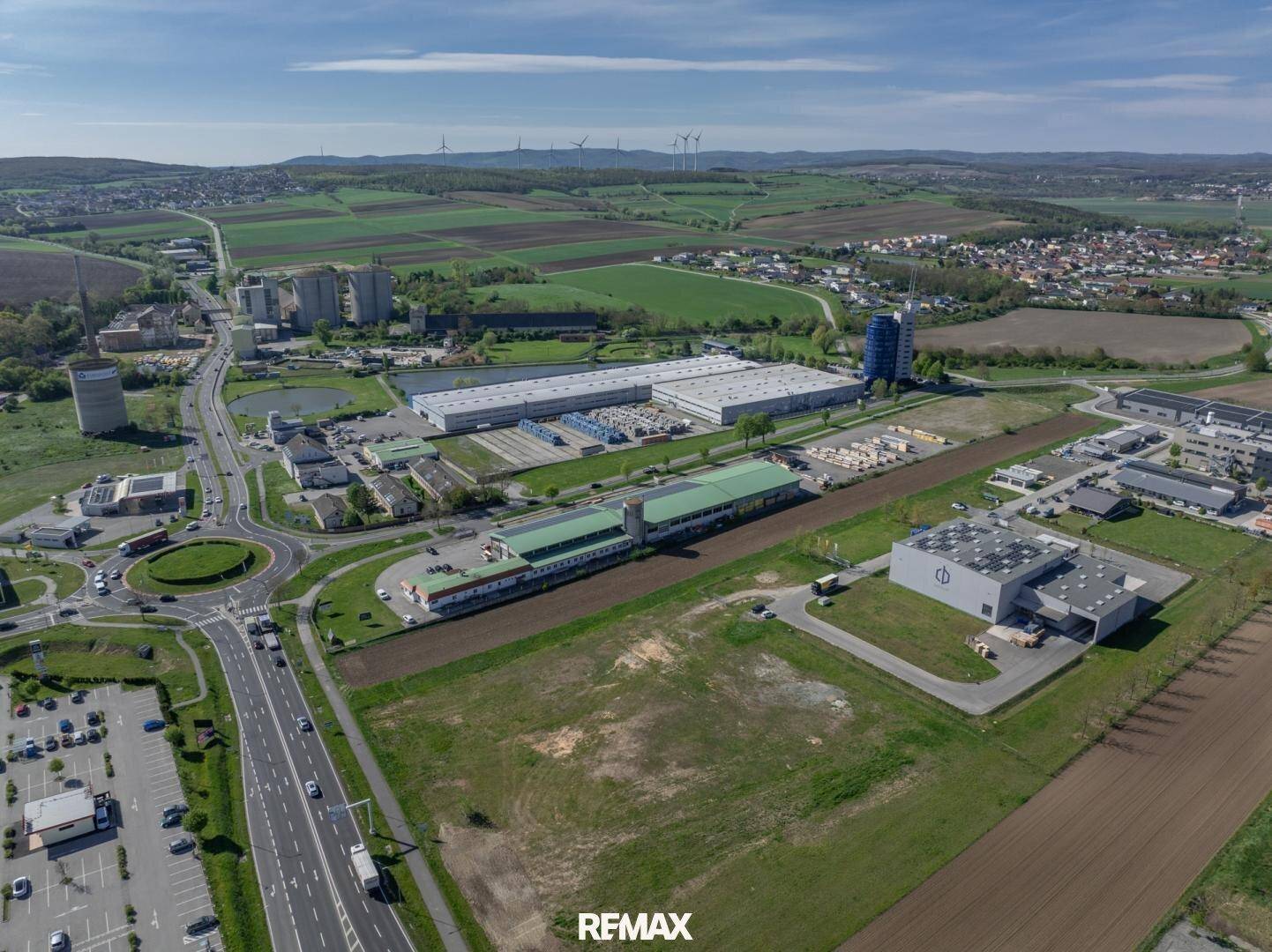 Weitwinkel-Luftaufnahme eines Gewerbegebiets mit Verkehrskreisel, Parkplätzen und Industrieanlagen.