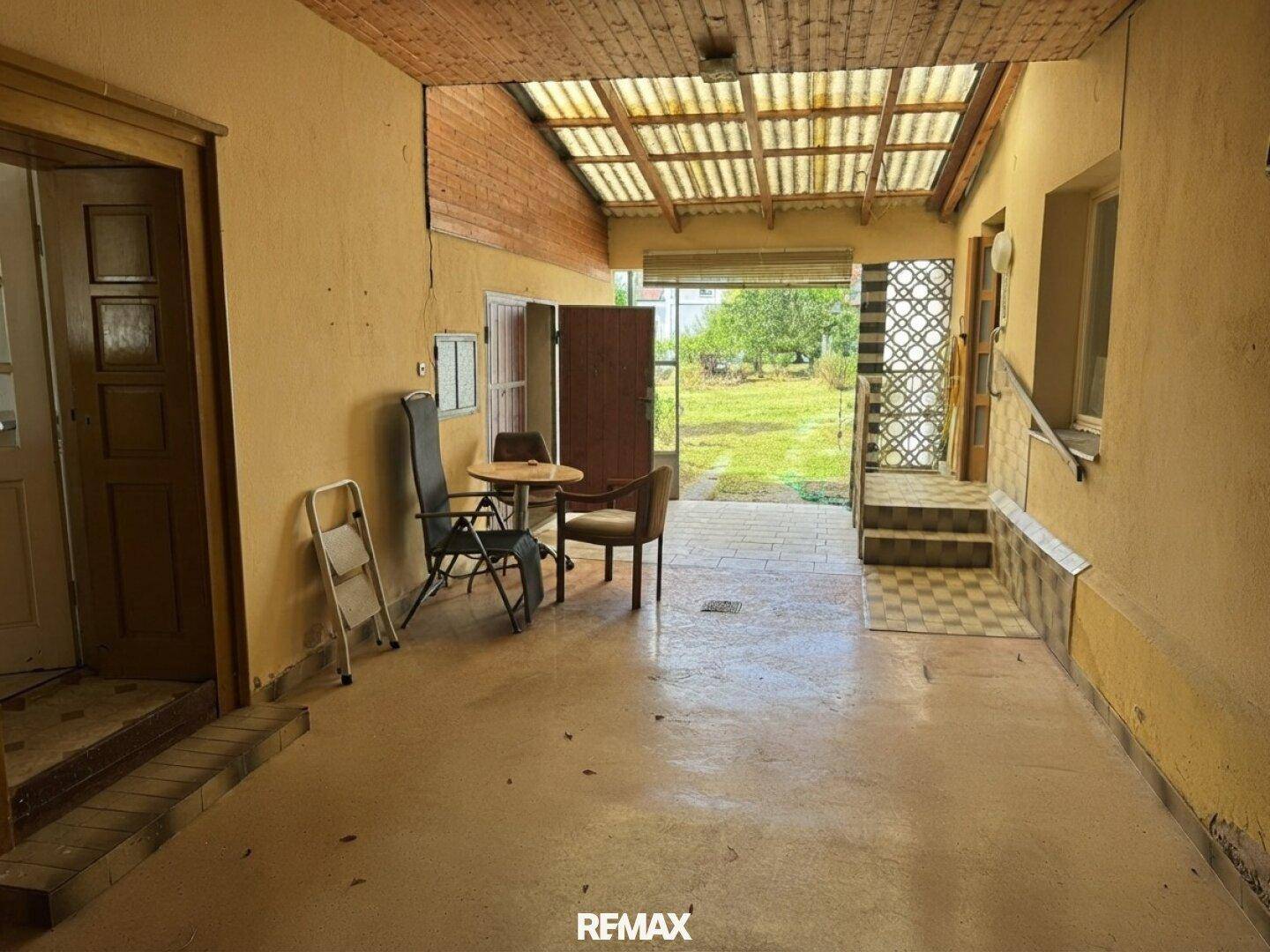 Heller, überdachter Bereich mit Fliesenboden und Blick in den grünen Garten.