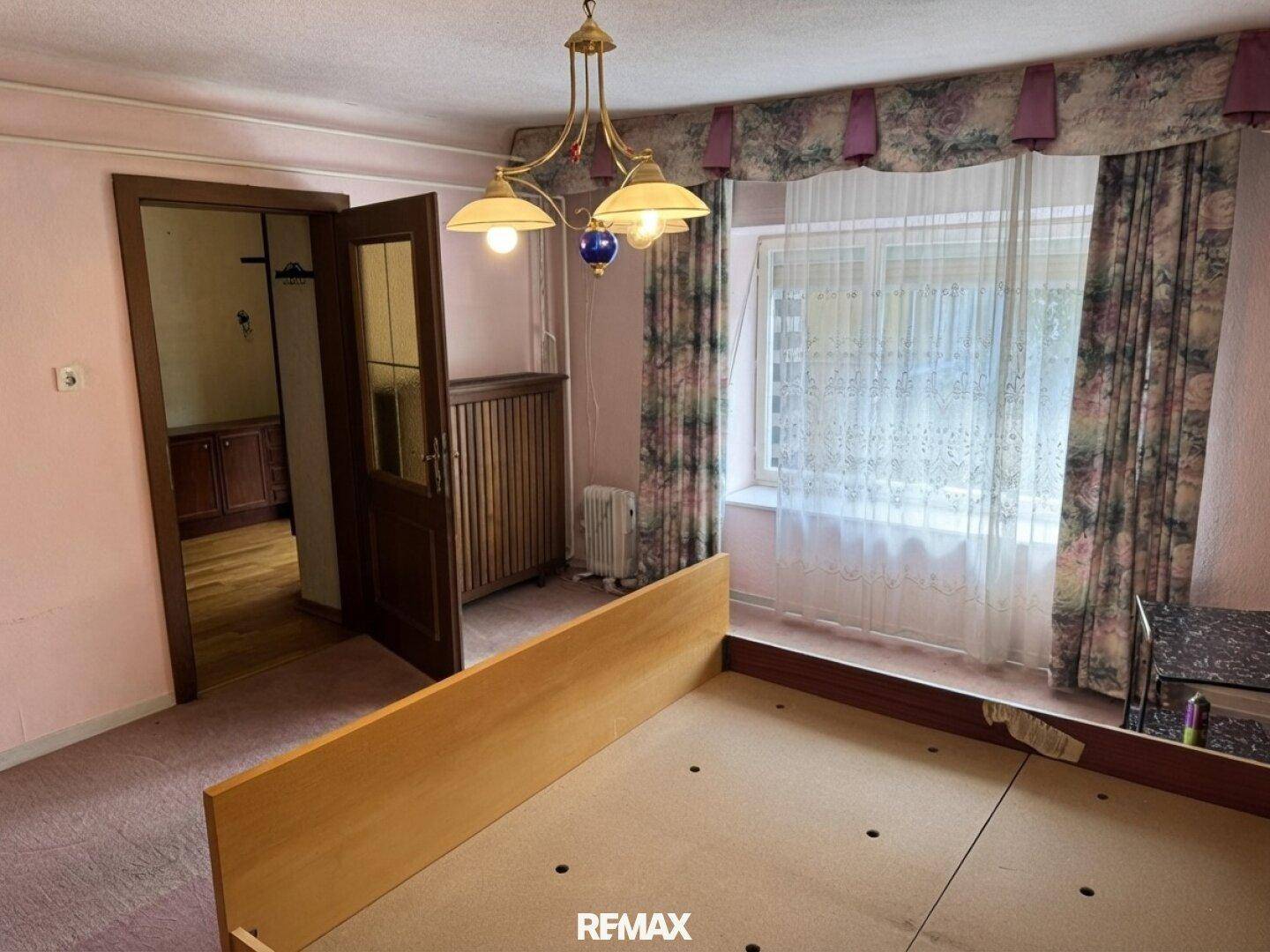 Schlafzimmer mit rosa Teppichboden, großen Fenstern und traditionellen Vorhängen.