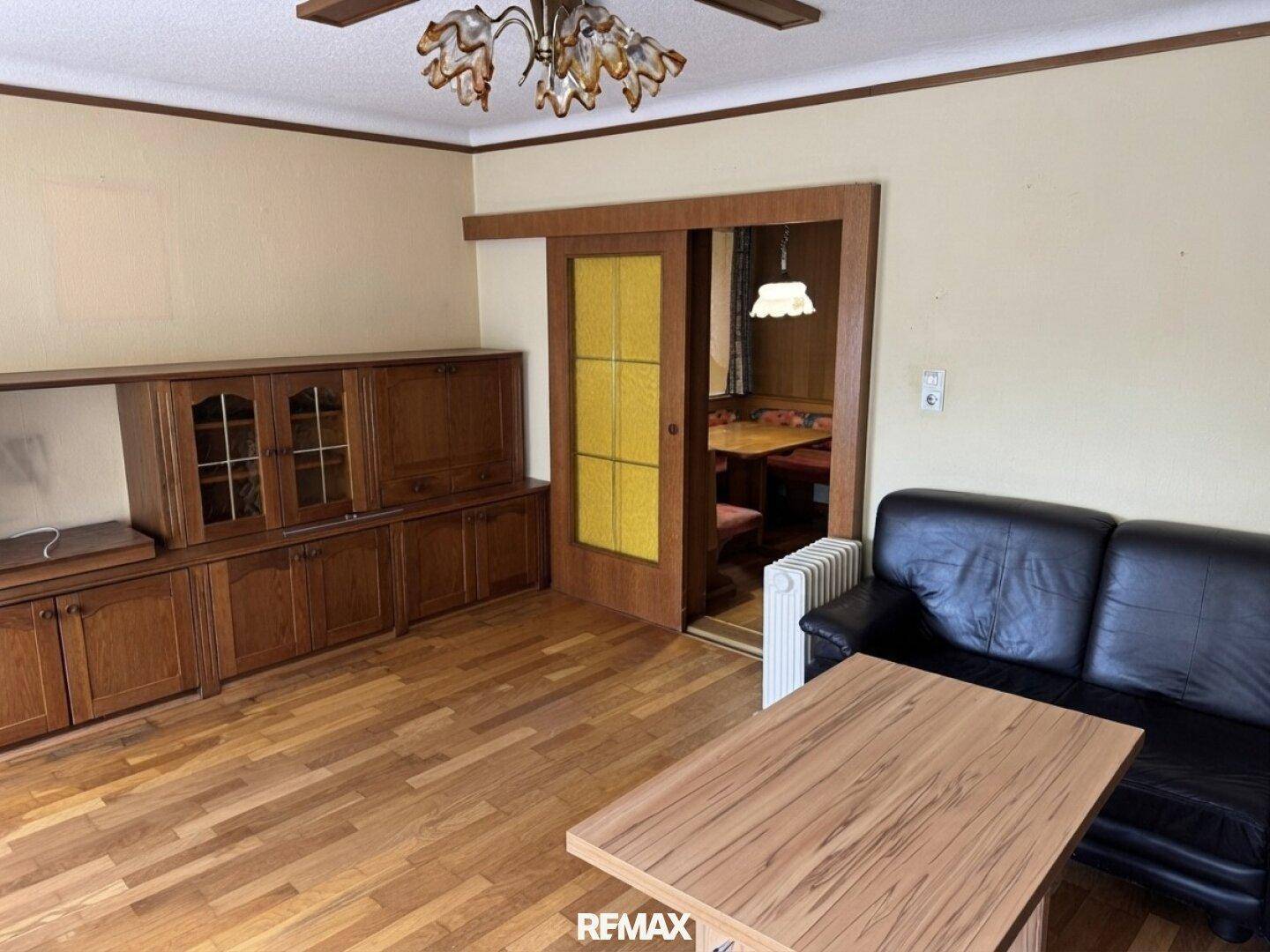 Wohnzimmer mit Holzparkett, dunklem Sofa und Schrankwand, verbunden mit Essbereich.