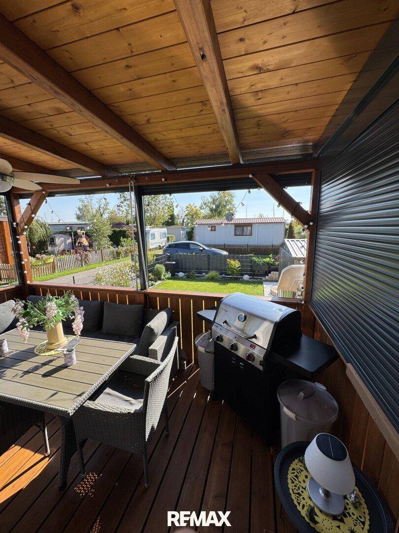 Gemütliche überdachte Terrasse mit Holzboden, Sitzgelegenheiten und einem Grill, ideal für Mahlzeiten im Freien.