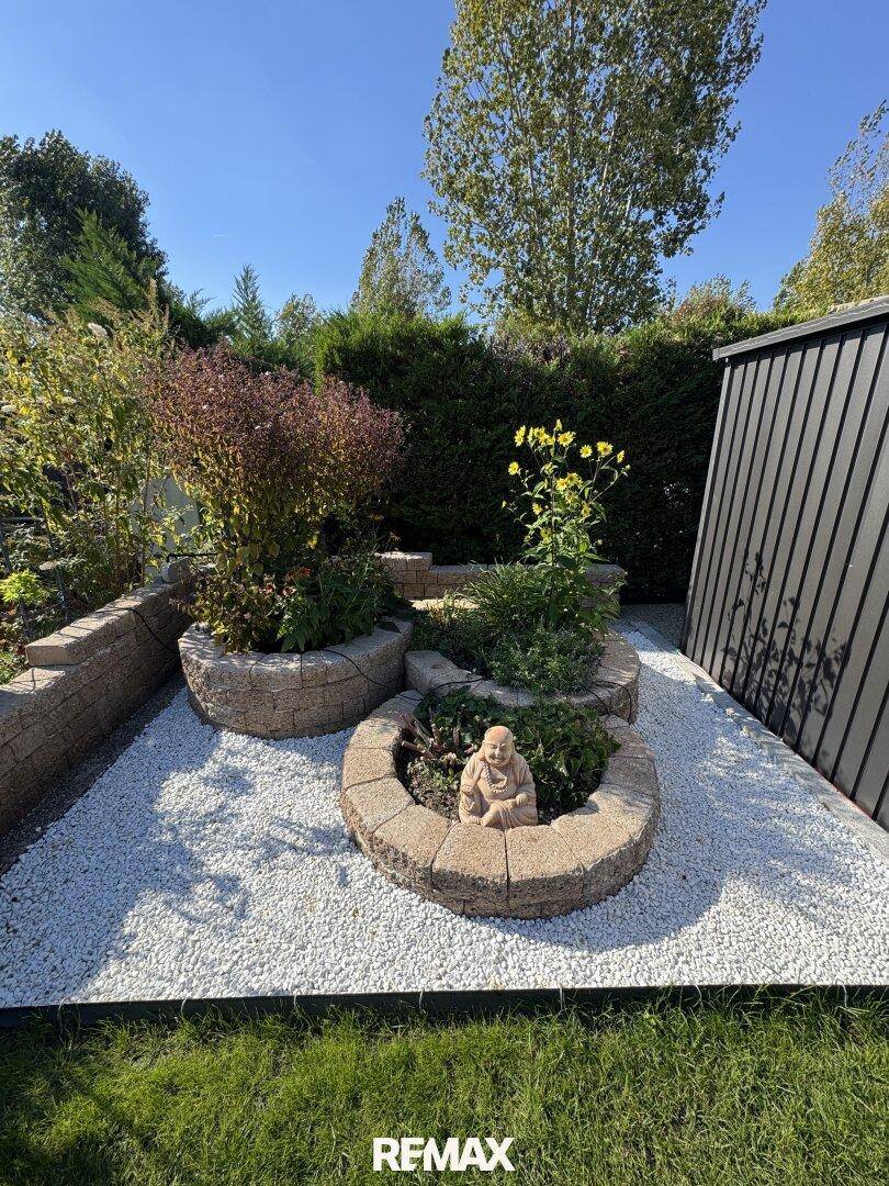 Detailansicht eines dekorativen Steingartens mit Pflanzen und einer Buddha-Statue im Garten.