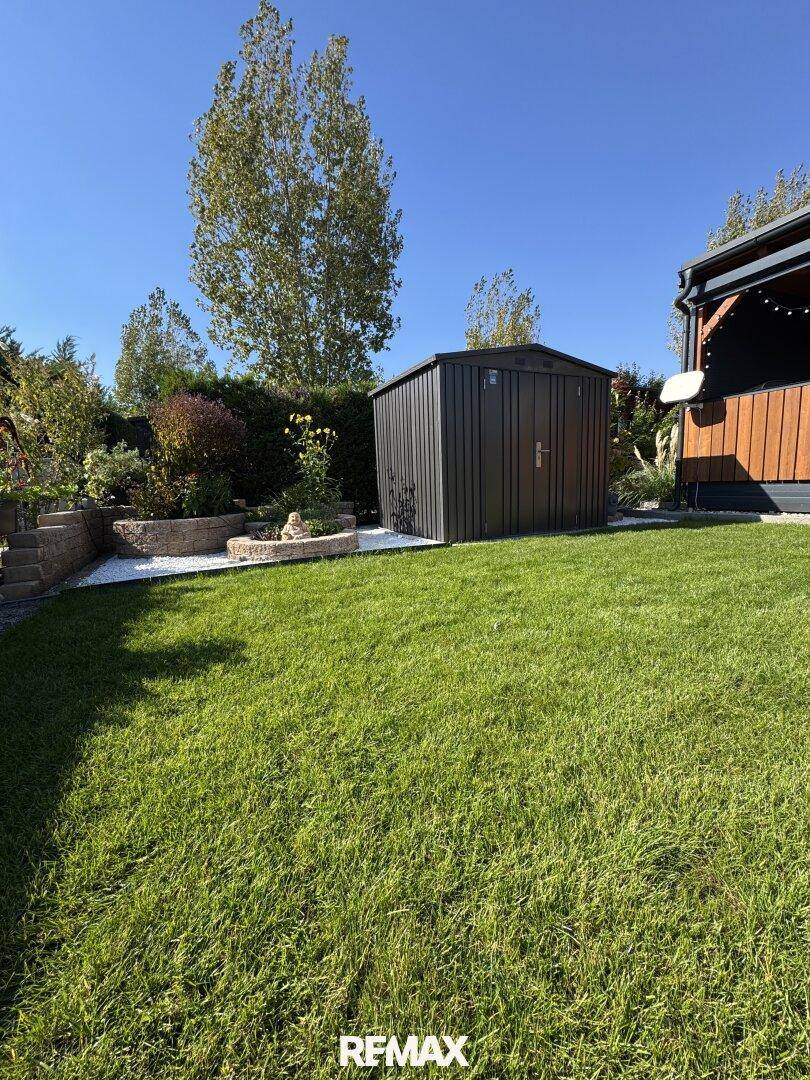Weitläufiger Rasenbereich im Garten mit einem praktischen Gartenhaus unter blauem Himmel.