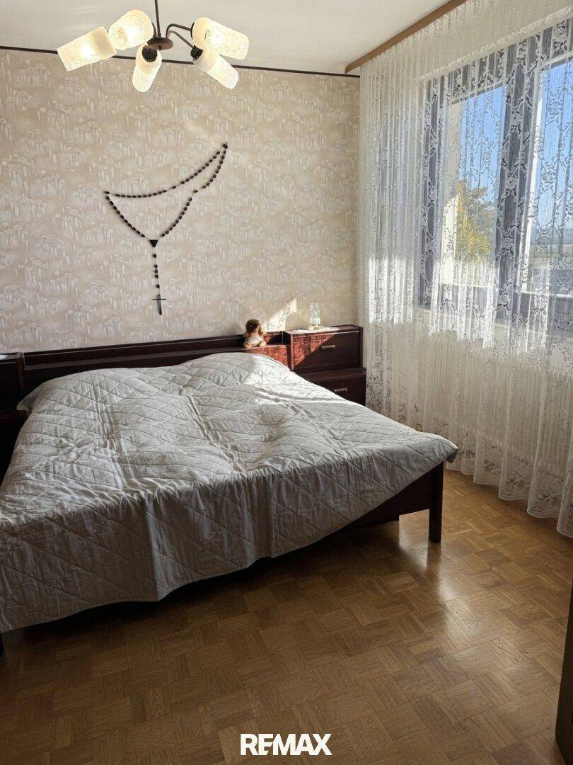 Schlafzimmer mit Parkettboden, Doppelbett und einem Fenster, das viel Tageslicht hereinlässt.