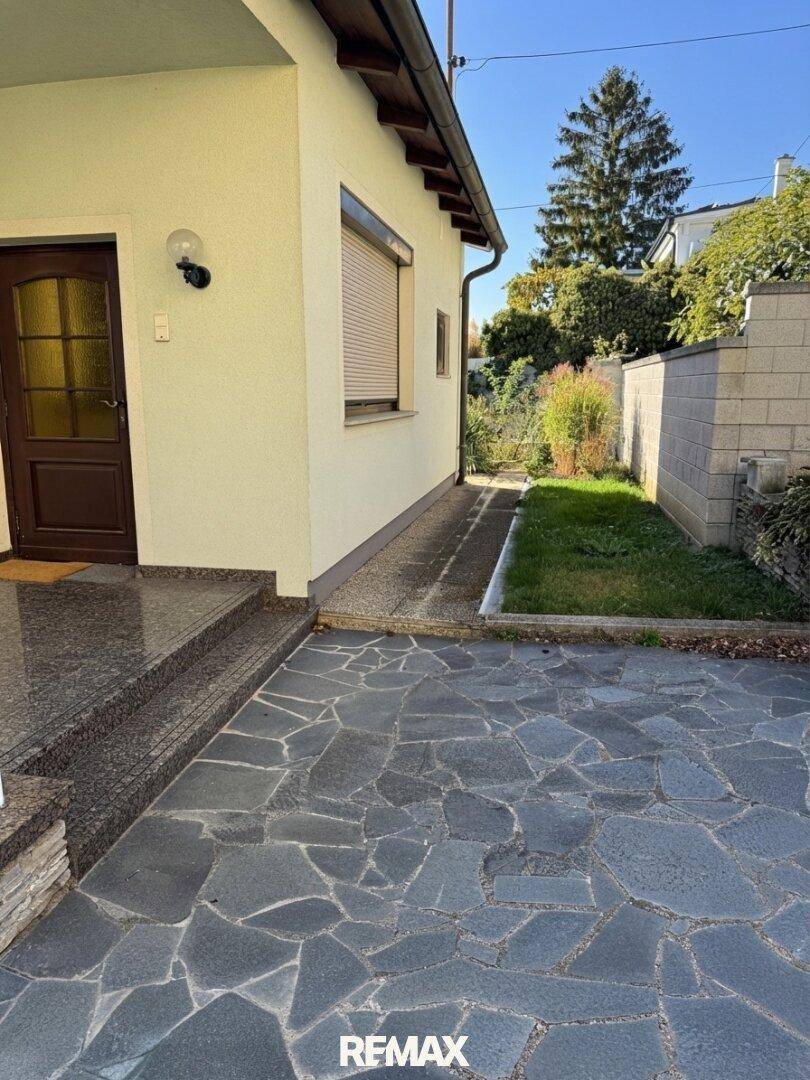 Seitlicher Eingangsbereich des Hauses mit dunkler Tür, Steinstufen und einer gepflasterten Fläche.
