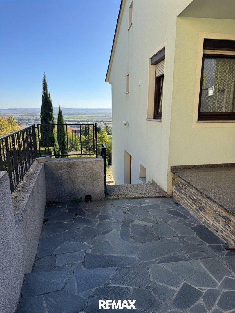 Seitliche Terrasse mit Steinfliesen und Treppen, die einen weiten Blick in die Landschaft ermöglichen.