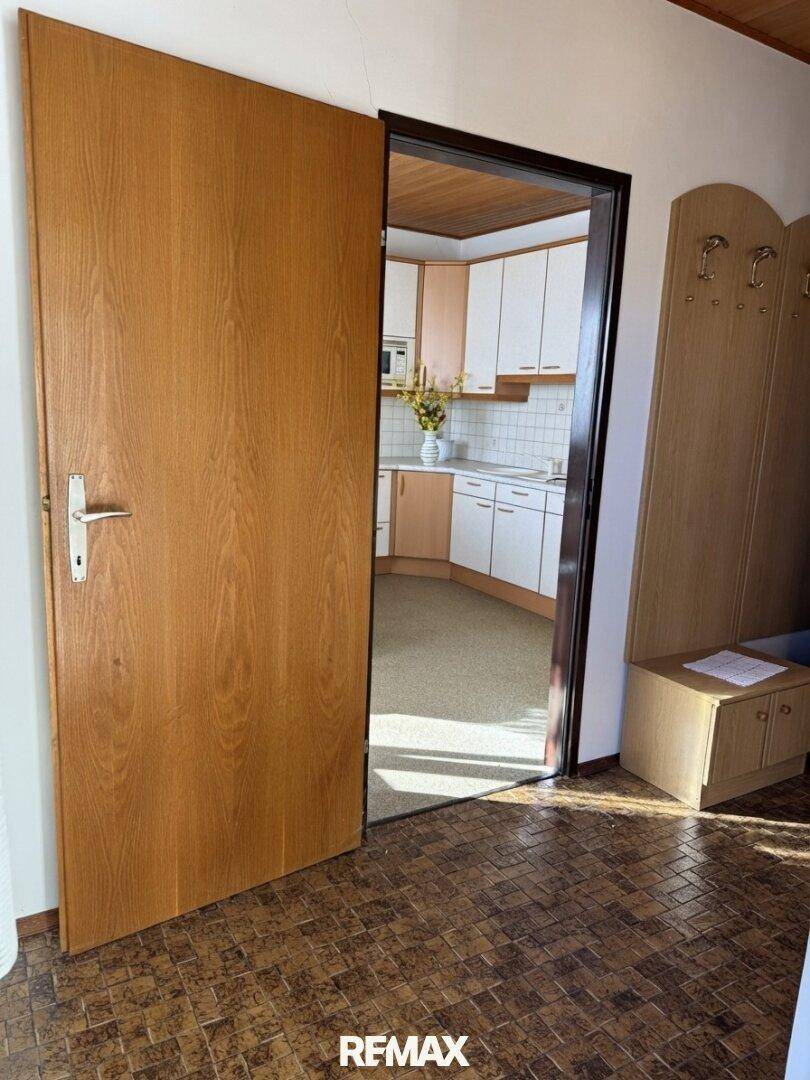 Heller Eingangsbereich mit Garderobe und einer Holztür, die in eine moderne Küche führt.