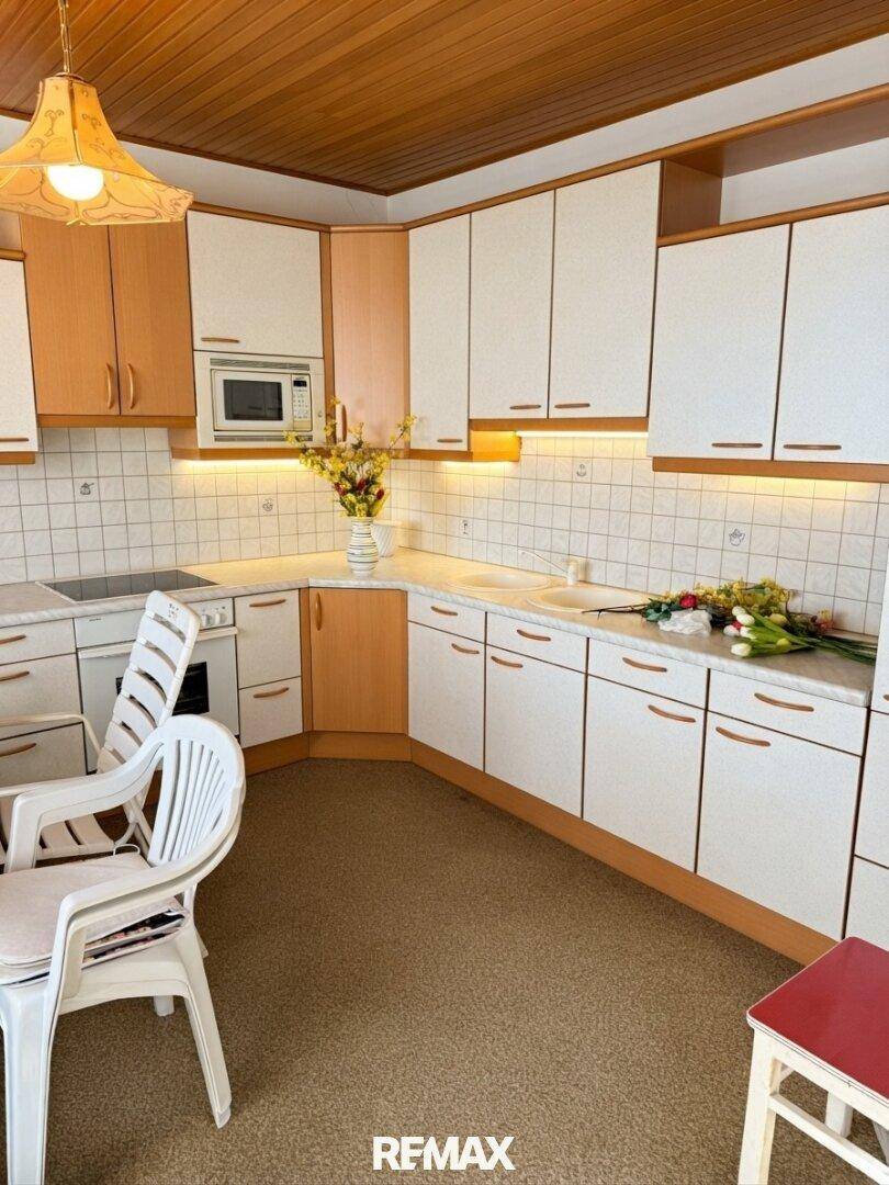 Helle Küche mit weißen und hellbraunen Schränken, Holzdecke und einem kleinen Essbereich.