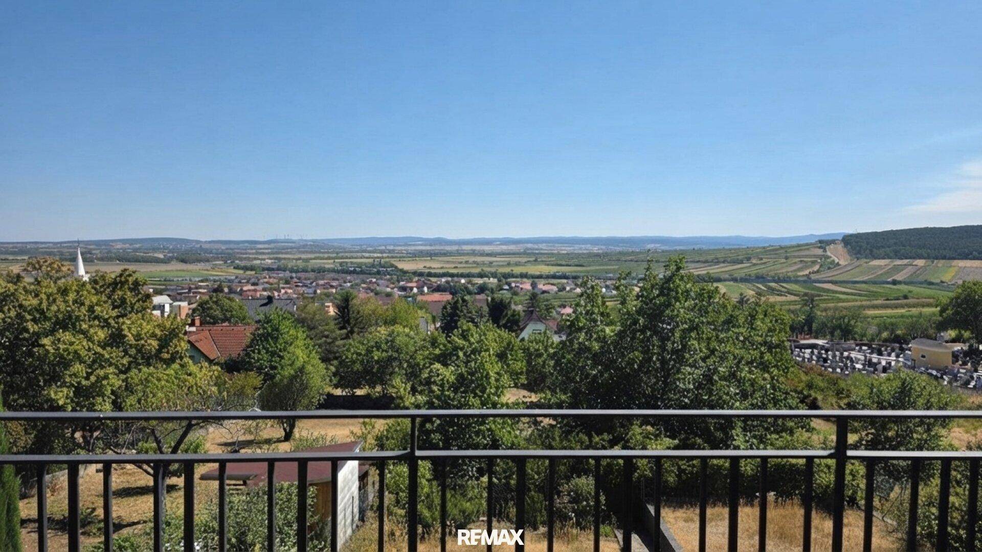 Weitläufiger Panoramablick über die Landschaft mit Feldern, Dörfern und einem Friedhof im Hintergrund.