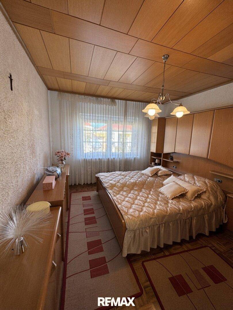 Schlafzimmer mit Holztäfelung an der Decke, Doppelbett und passenden Holzkommoden, hell durch großes Fenster.