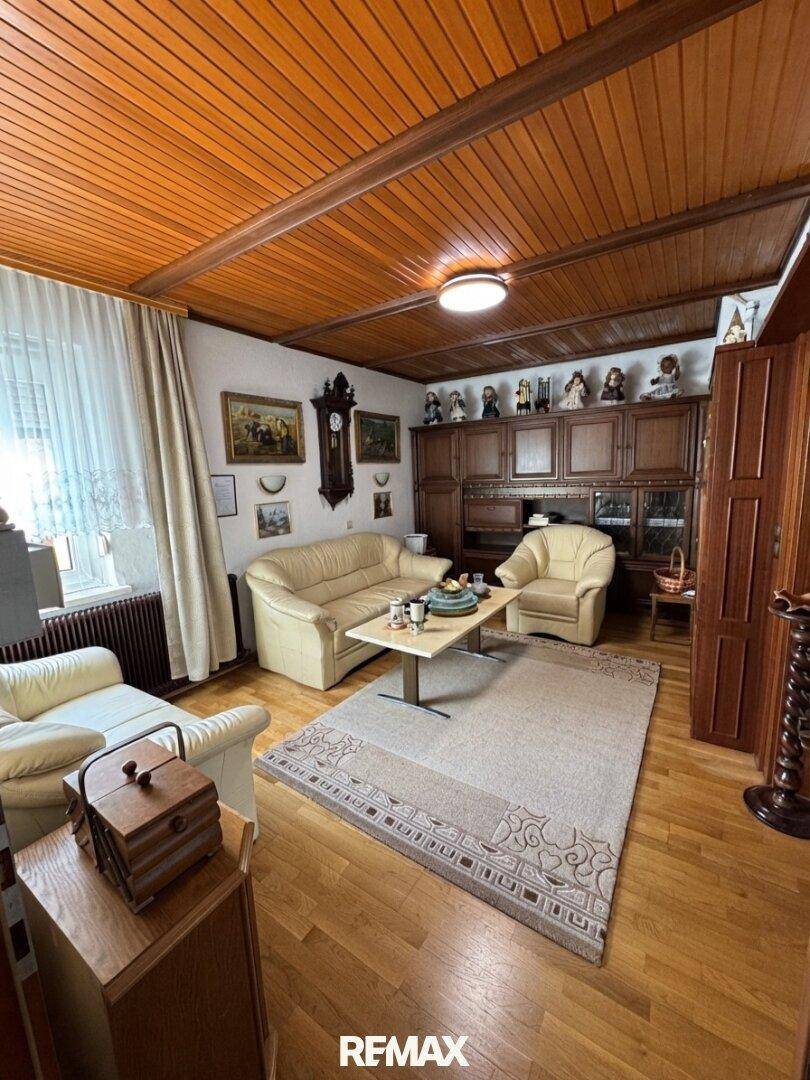 Gemütliches Wohnzimmer mit Holztäfelung an der Decke, beigen Sofas und traditionellen Holzmöbeln, gut beleuchtet.