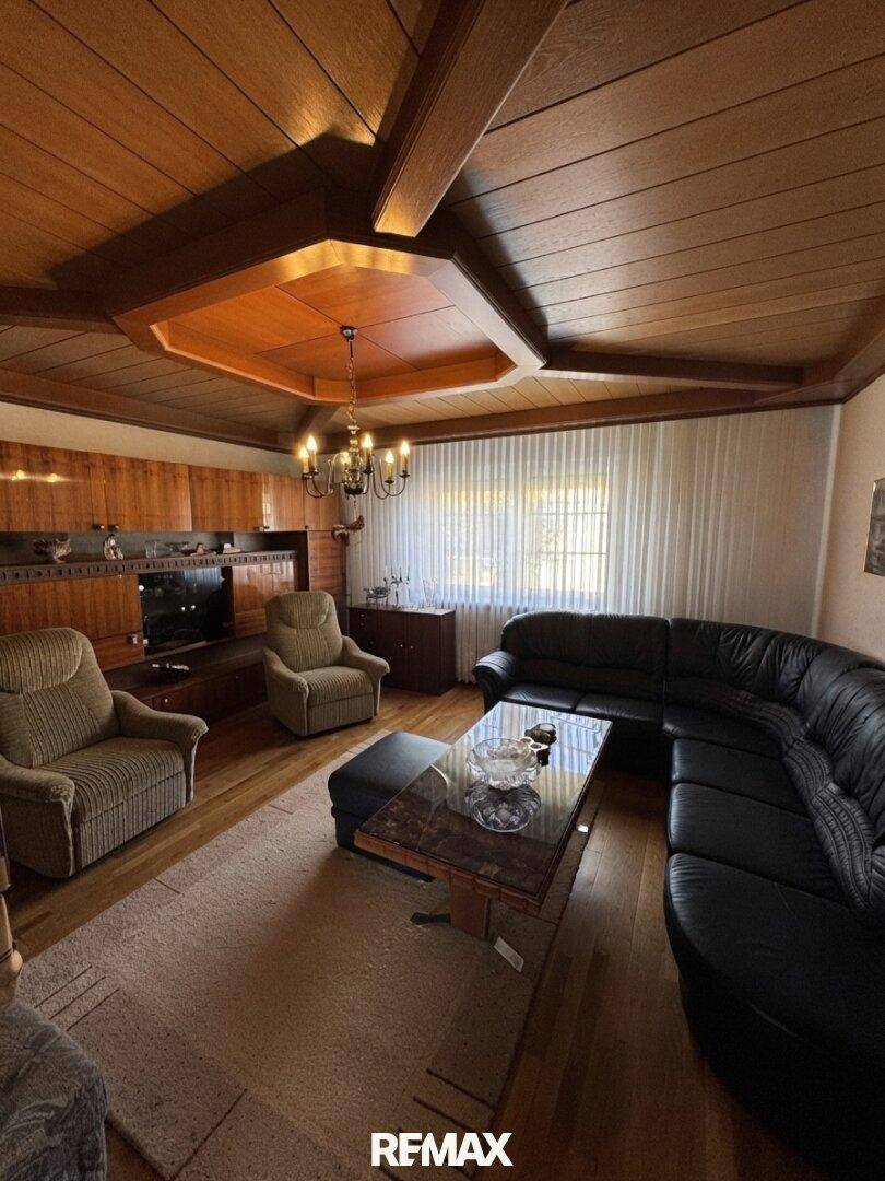 Geräumiges Wohnzimmer mit Holztäfelung, dunklem Ledersofa und einem Couchtisch mit eleganter Marmorplatte.