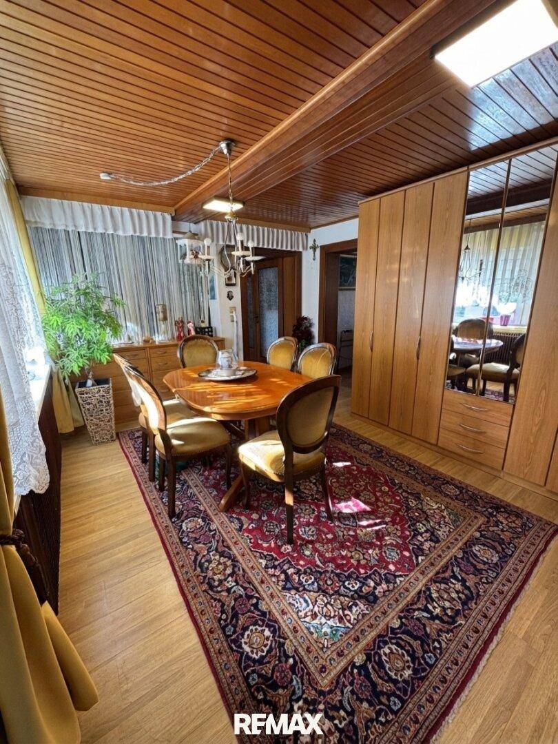 Heller Essbereich mit Holztäfelung an der Decke, rundem Holztisch und Spiegelschränken, die den Raum erweitern.