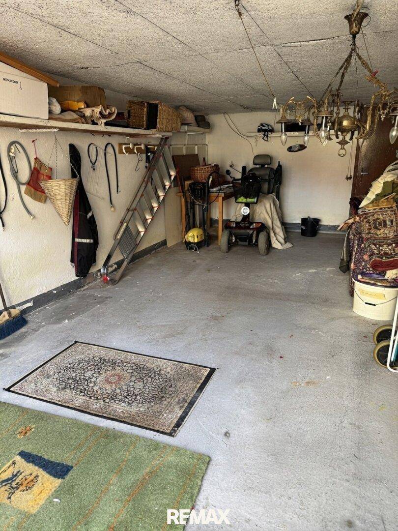 Geräumige Garage mit Betonboden, Leiter und verschiedenen Lagergegenständen, funktional eingerichtet.