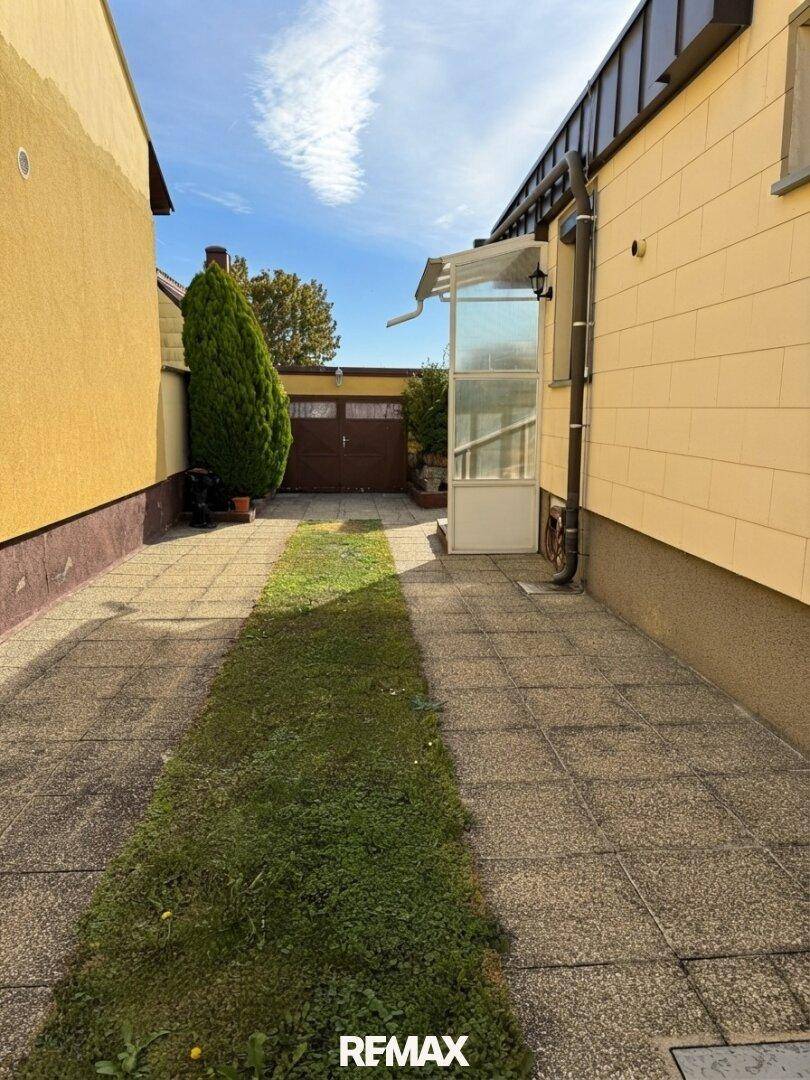 Einfahrt zum Haus mit gepflastertem Weg und Rasenstreifen, führt direkt zur Garage im Hintergrund.