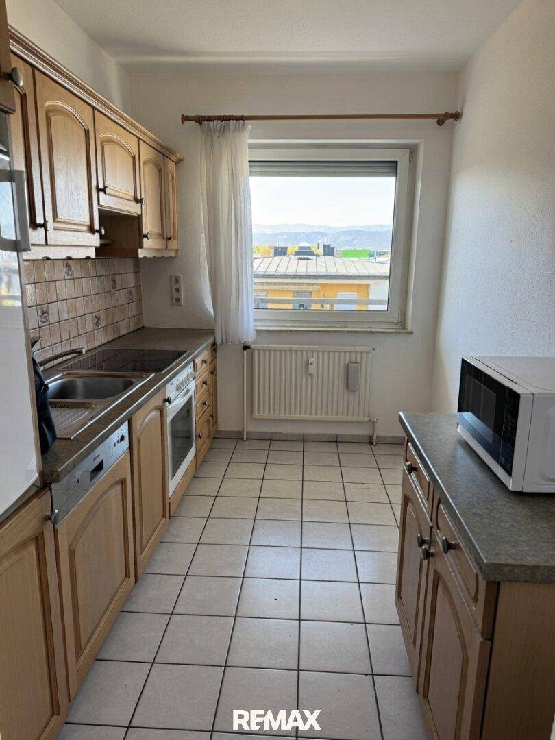 Funktionale Küche mit hellen Holzschränken, Fliesenboden und einem Fenster mit Ausblick.