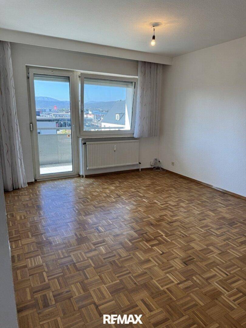 Geräumiges Zimmer mit Parkettboden, großem Fenster und Zugang zu einem Balkon.