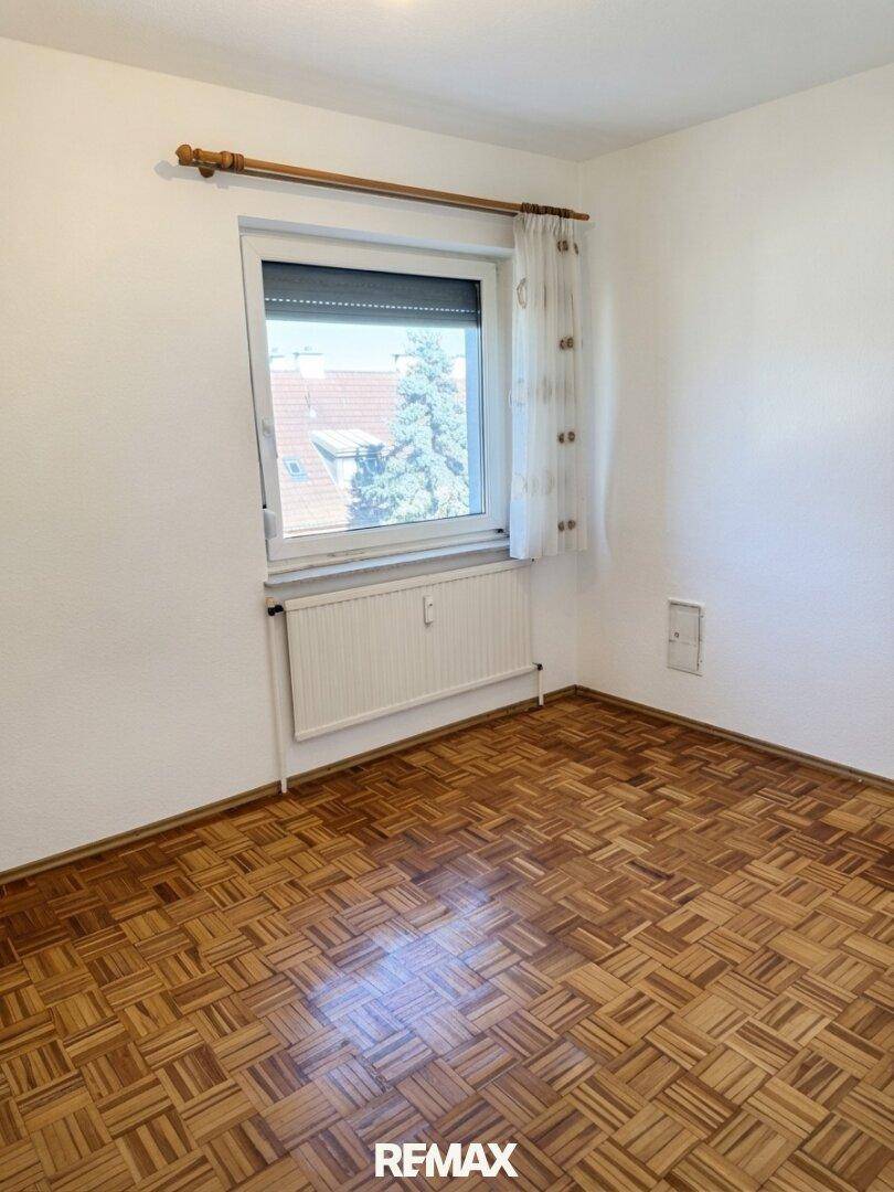 Gemütliches Zimmer mit Parkettboden und einem Fenster, das Tageslicht hereinlässt.