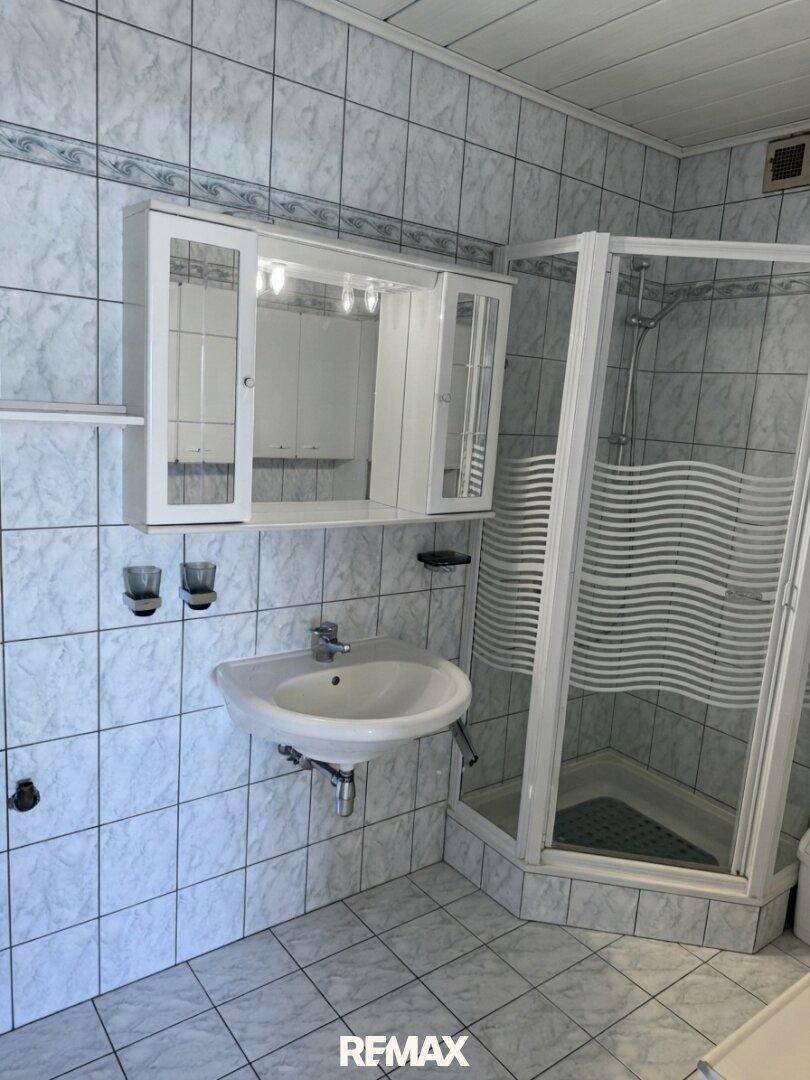 Gefliestes Badezimmer mit Waschbecken, Spiegelschrank und einer Eckdusche.