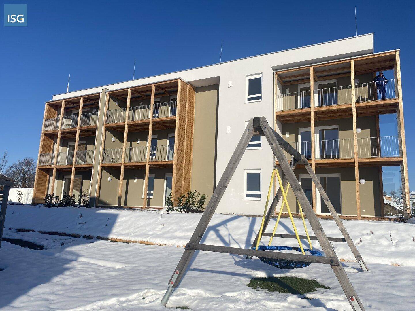 Modernes Mehrfamilienhaus mit Balkonen und einem Spielplatz im verschneiten Außenbereich.