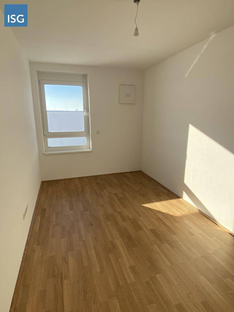 Leeres Schlafzimmer mit Holzboden und einem Fenster, das viel Tageslicht hereinlässt.