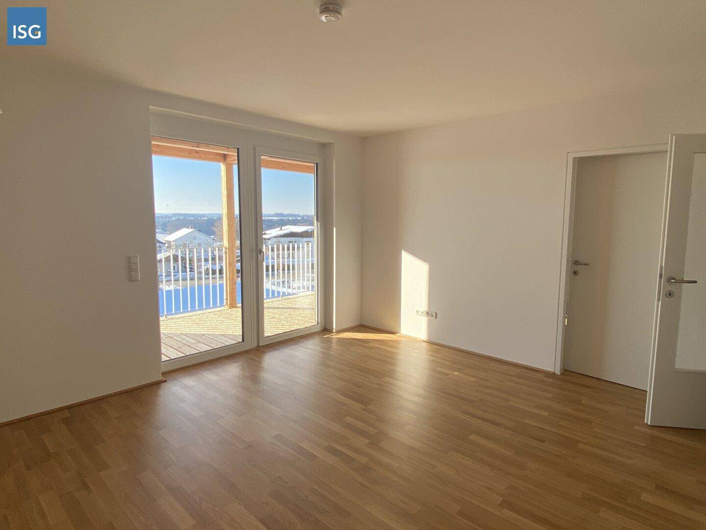 Heller, leerer Raum mit Holzboden und Zugang zu einem sonnigen Balkon.