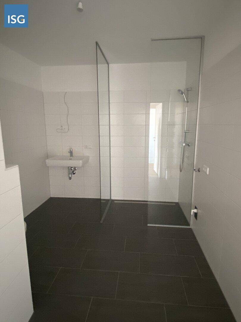 Modernes Badezimmer mit ebenerdiger Dusche, Waschbecken und dunklen Bodenfliesen.