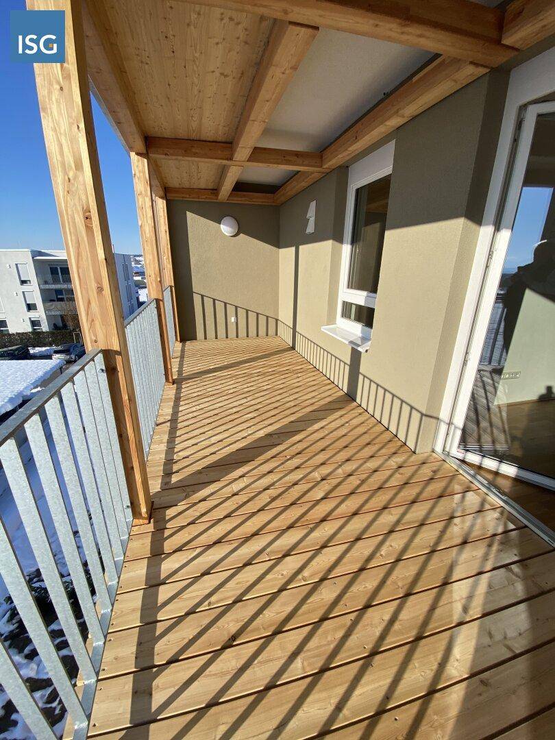 Geräumiger Balkon mit Holzboden und Metallgeländer, ideal für sonnige Stunden.