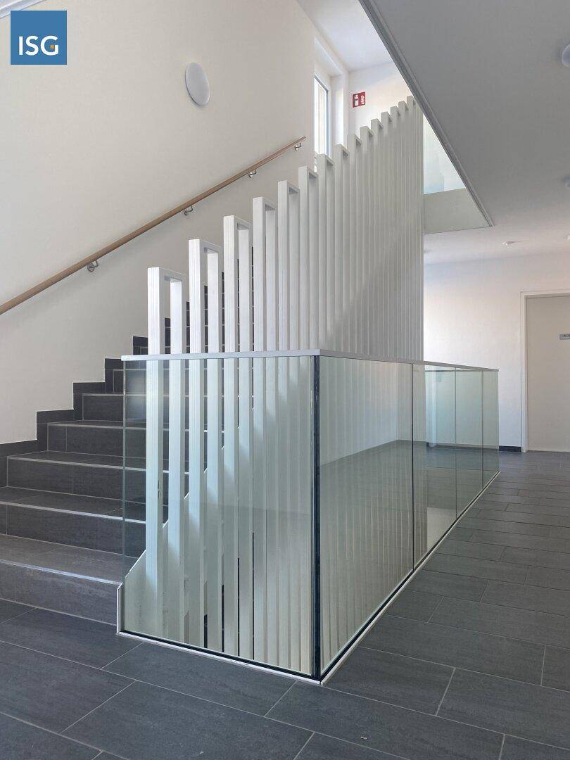 Modernes Treppenhaus mit Glasgeländer und vertikalen Lamellen, hell und einladend.