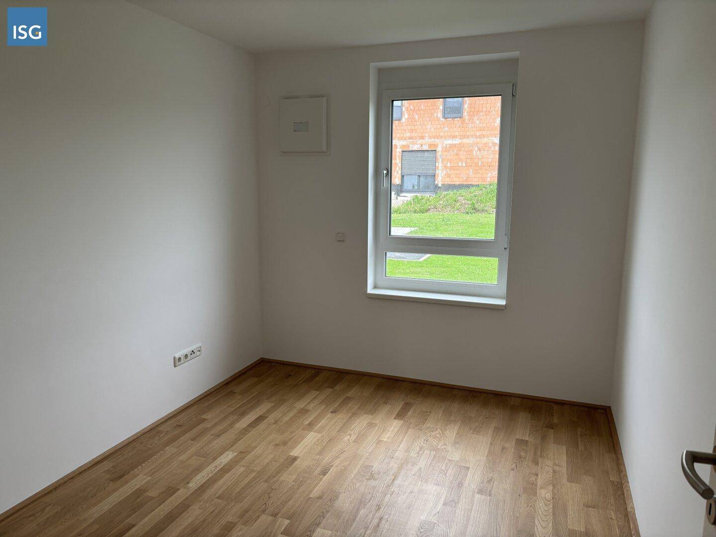 Leeres Schlafzimmer mit Parkettboden und einem Fenster, das für ausreichend Tageslicht sorgt.