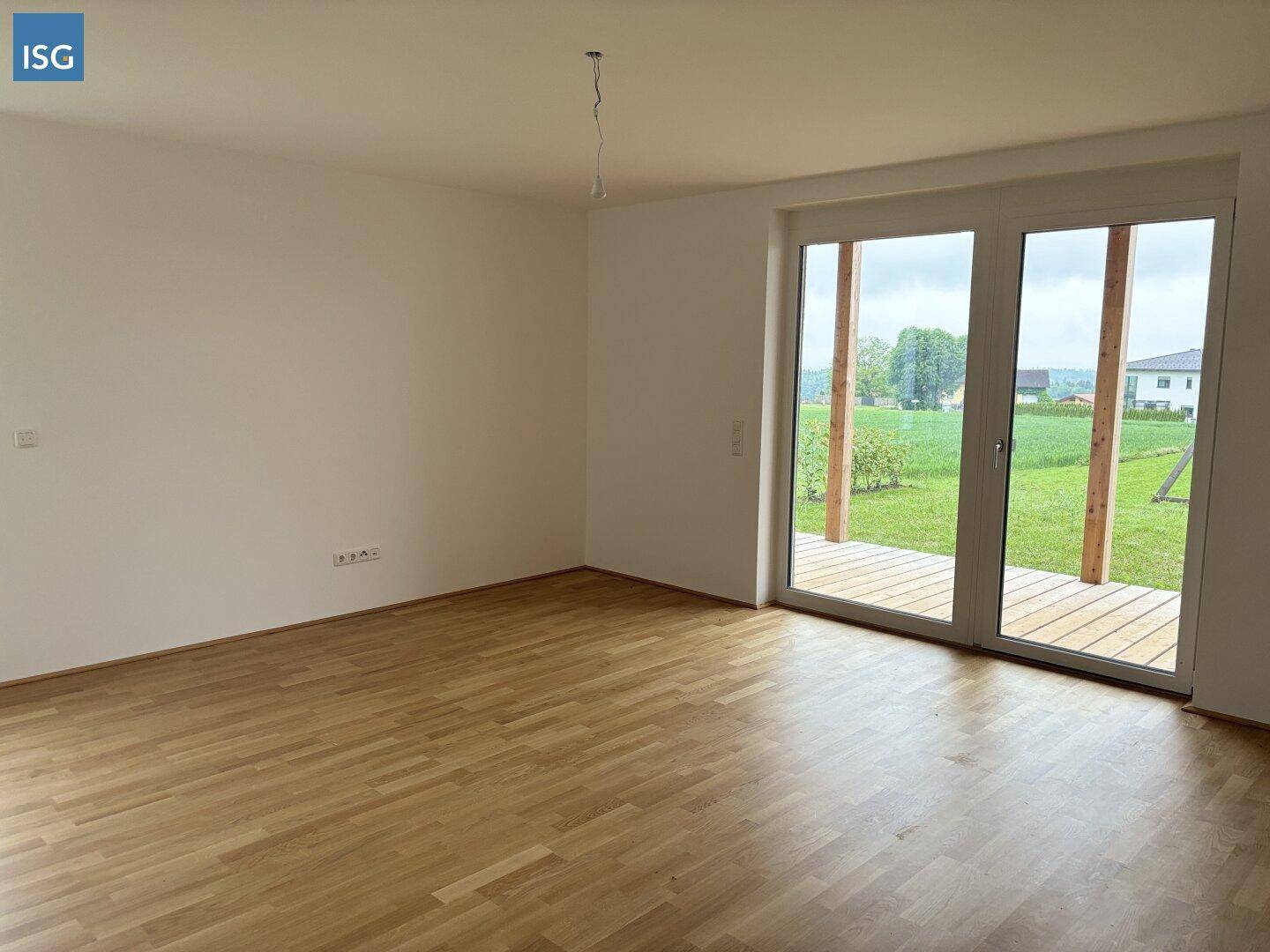 Heller Wohnraum mit Parkettboden und großzügigem Zugang zu einer Holzterrasse mit Grünblick.