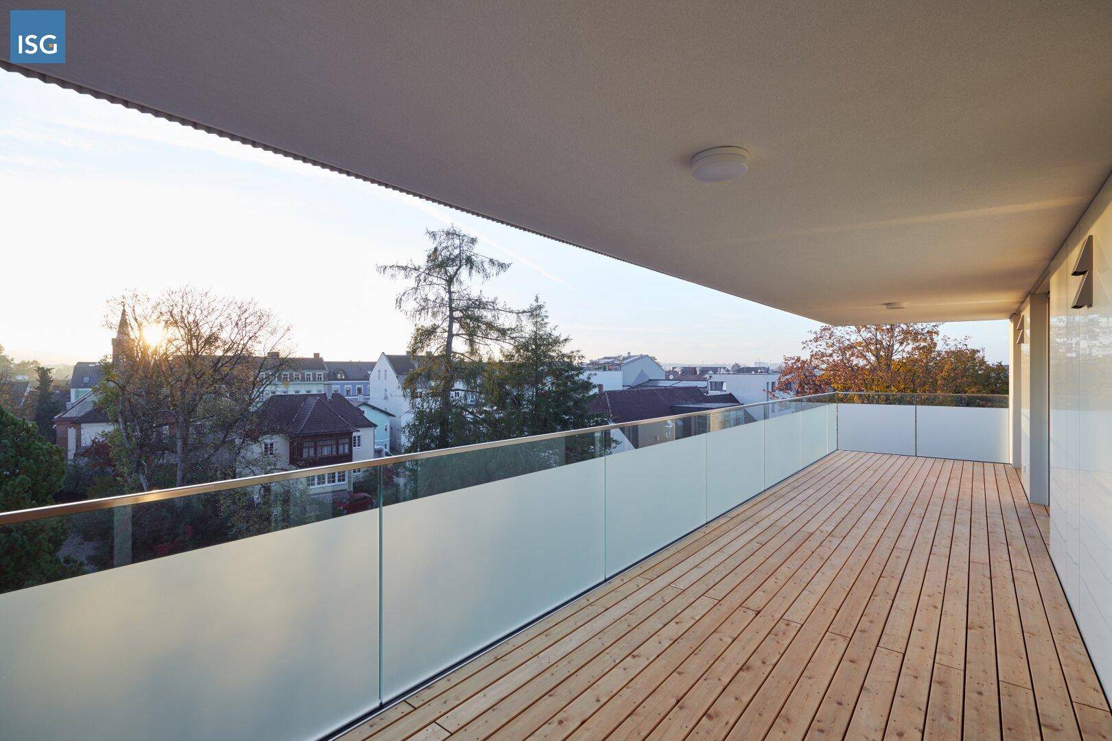 Geräumiger Balkon mit Holzboden und Glasgeländer, bietet einen weiten Blick über die Stadt.
