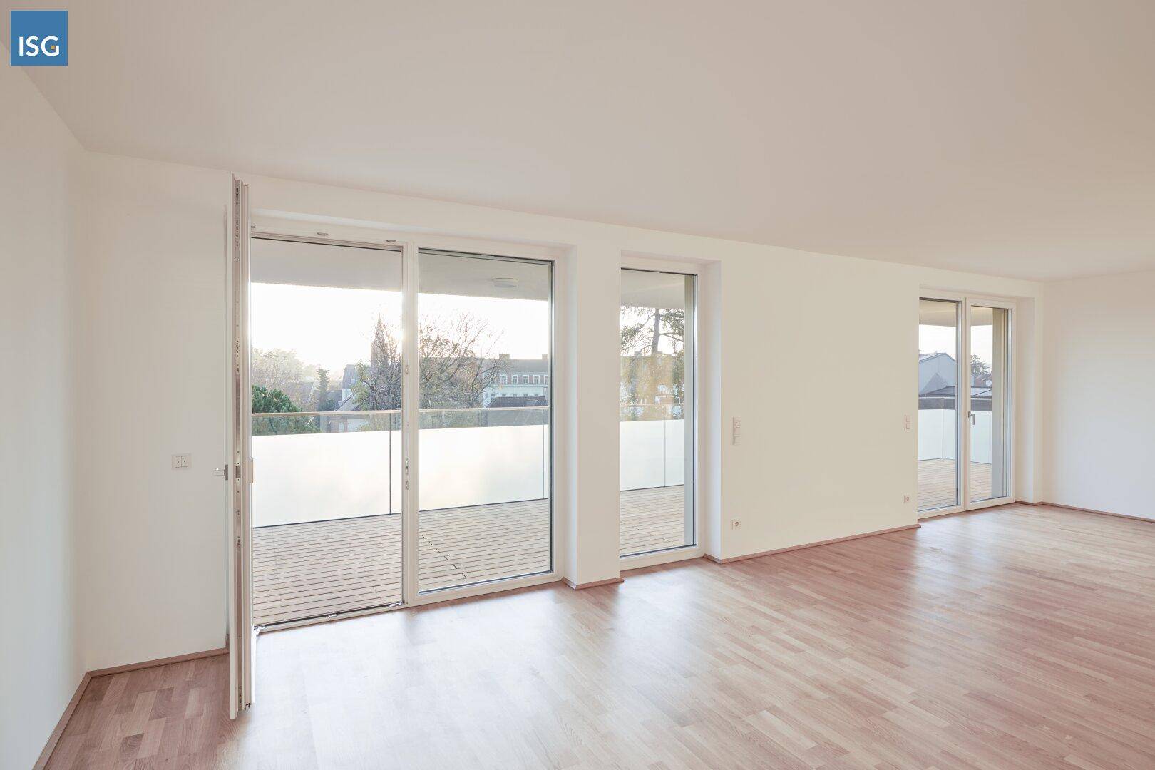 Heller, leerer Raum mit Holzboden und großen Schiebetüren, die zu einem Balkon führen.
