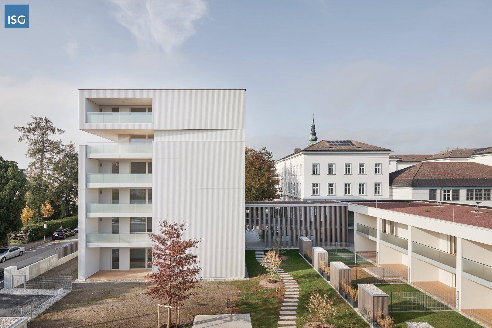 Modernes Wohngebäude mit weißer Fassade und Balkonen, umgeben von einem angelegten Gartenbereich.