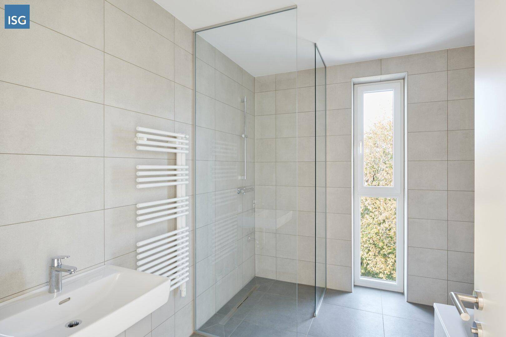 Modernes Badezimmer mit großen hellen Fliesen, ebenerdiger Dusche und Fenster.