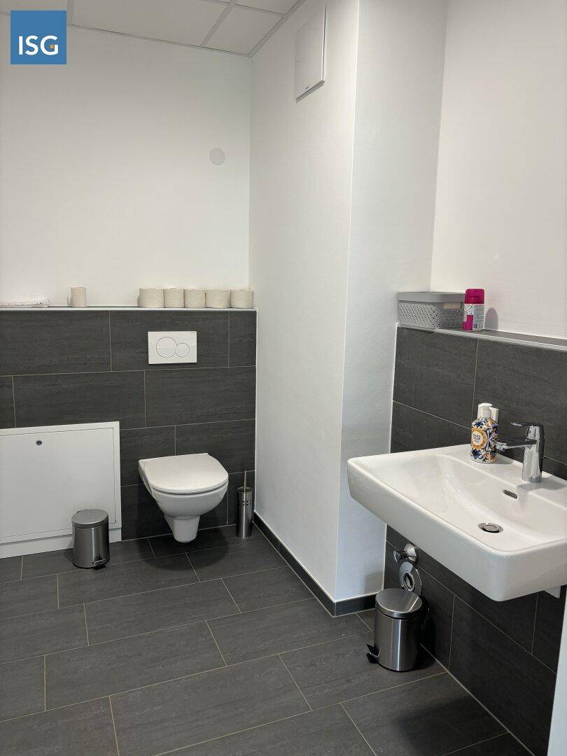 Modernes WC mit dunklen Fliesen, wandhängender Toilette und einem weißen Waschbecken.