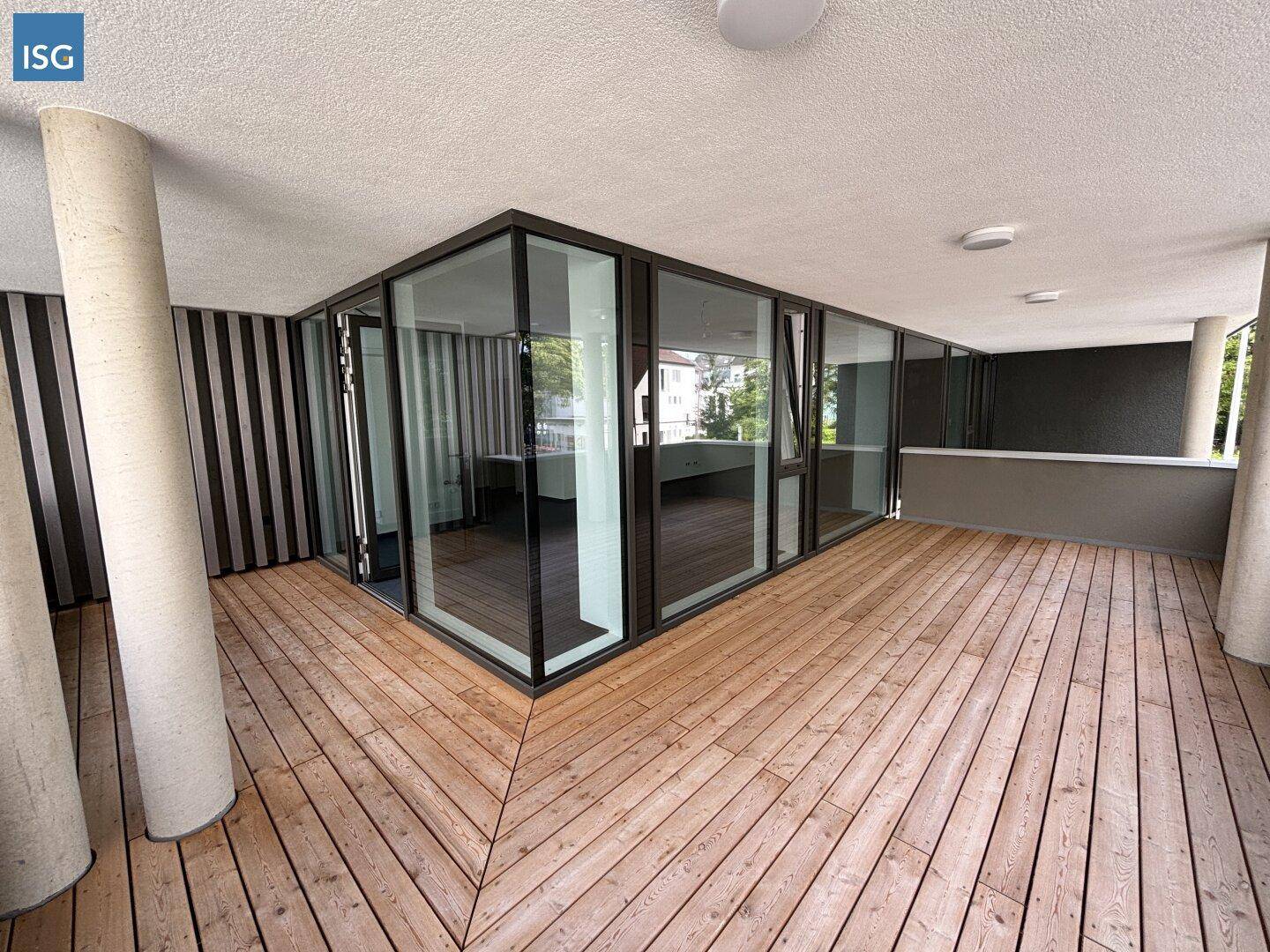 Geräumige Loggia mit Holzfußboden und großen Glasfronten, die viel natürliches Licht hereinlassen.