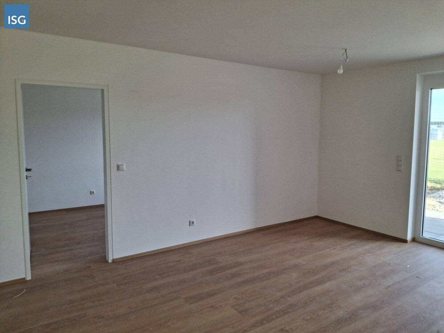 Heller, leerer Wohnraum mit Laminatboden und Zugang zu einem Außenbereich.