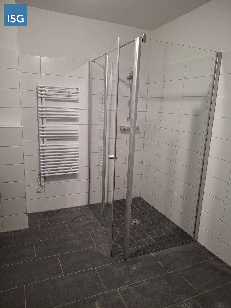 Modernes Badezimmer mit ebenerdiger Dusche, weißen Fliesen und beheiztem Handtuchhalter.