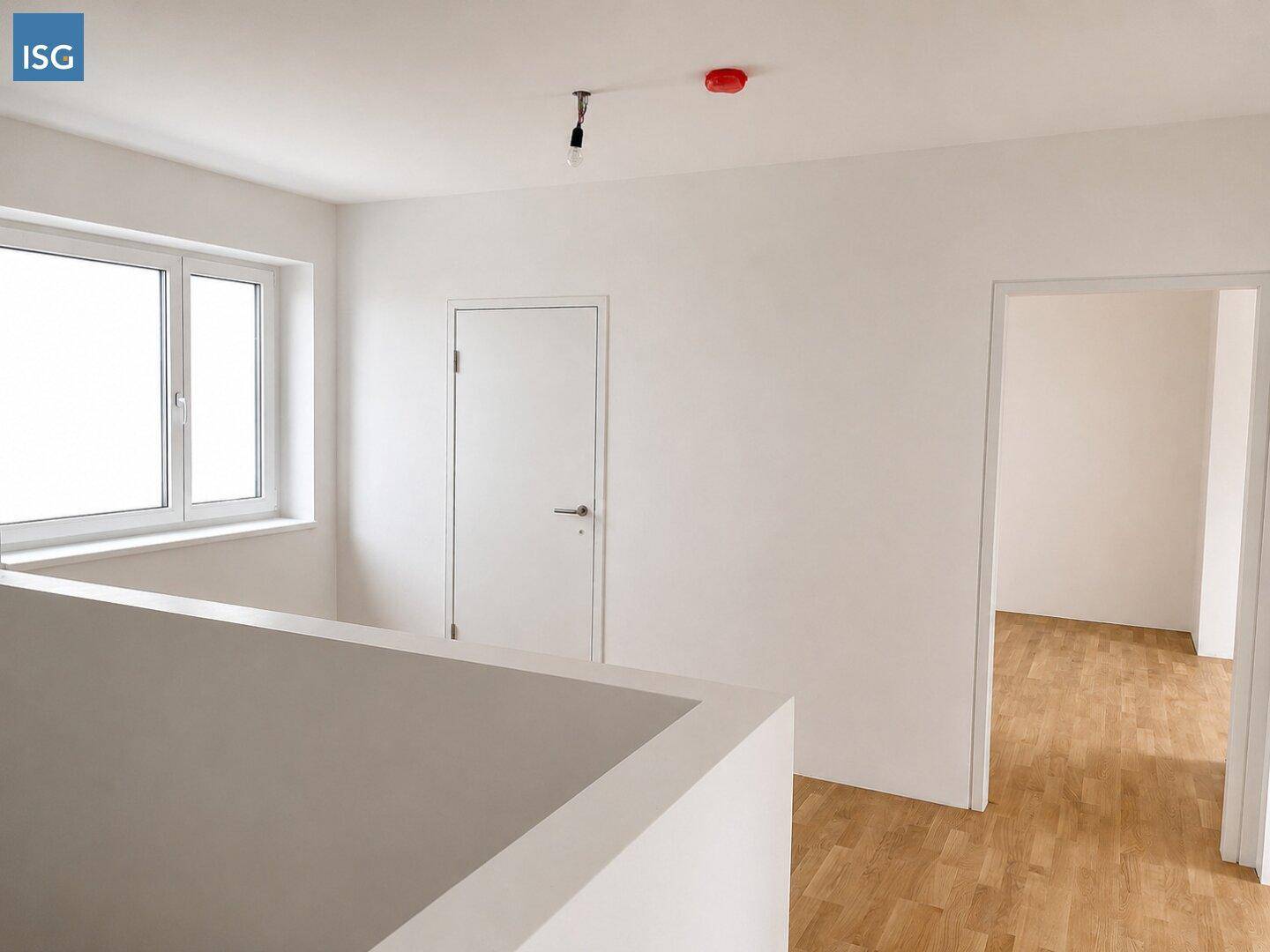 Heller Flurbereich mit Fenster und Holzboden, der zu weiteren Zimmern im Neubau führt.