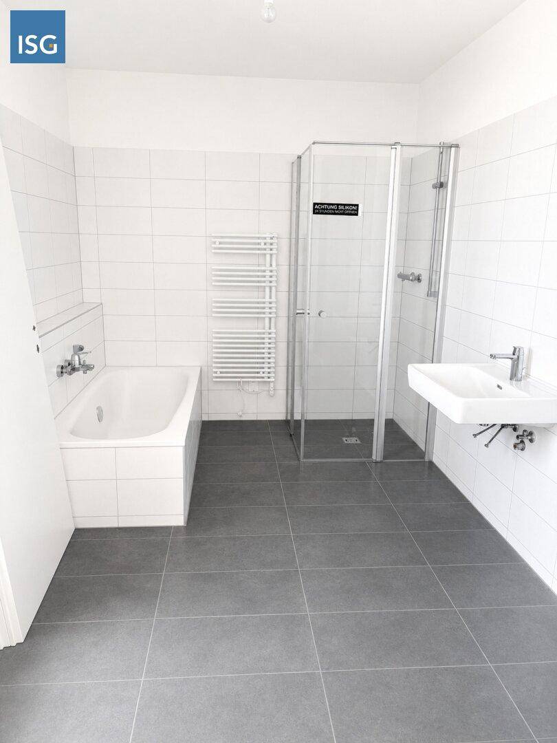 Modernes Badezimmer mit Badewanne, Duschkabine, Handtuchheizkörper und grauen Bodenfliesen.