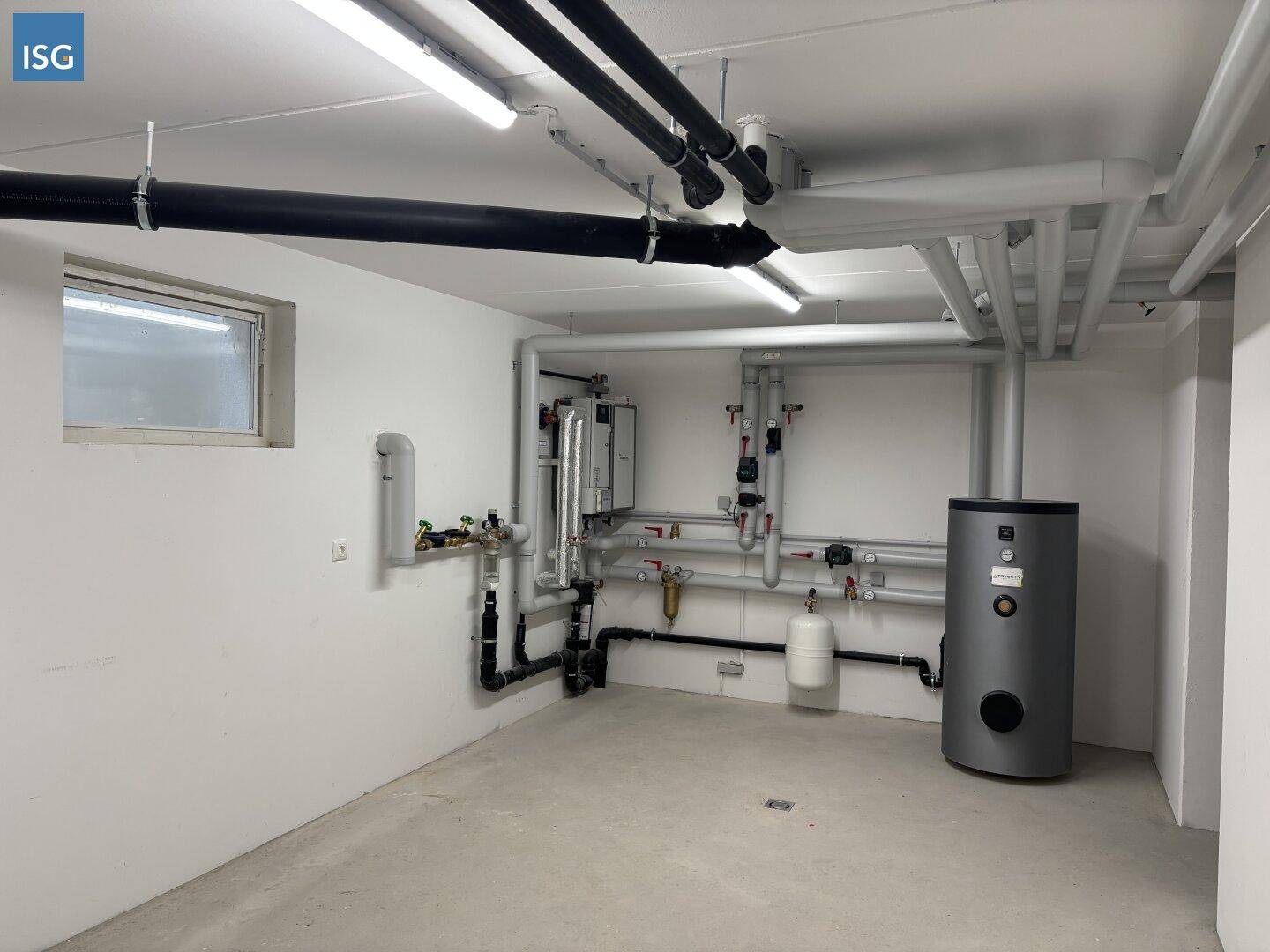 Technikraum im Keller mit Heizungsanlage, Warmwasserspeicher und sichtbaren Rohrleitungen.