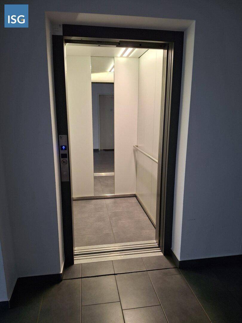 Moderner Aufzug mit Spiegelflächen und dunklen Fliesen im Eingangsbereich des Gebäudes.