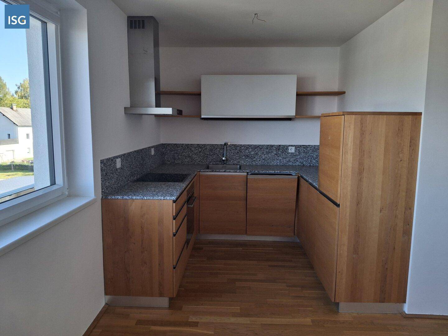 Moderne Einbauküche mit Holzfronten, Granitarbeitsplatte und Fenster mit Blick ins Grüne.