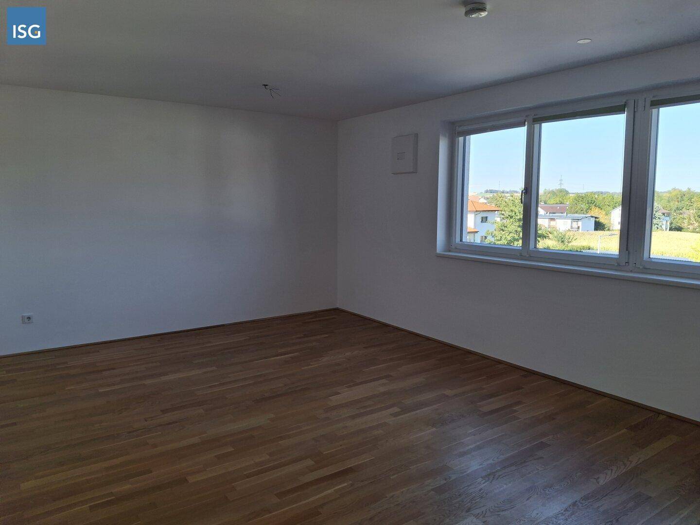 Helles, leeres Zimmer mit Parkettboden und großen Fenstern mit Weitblick.