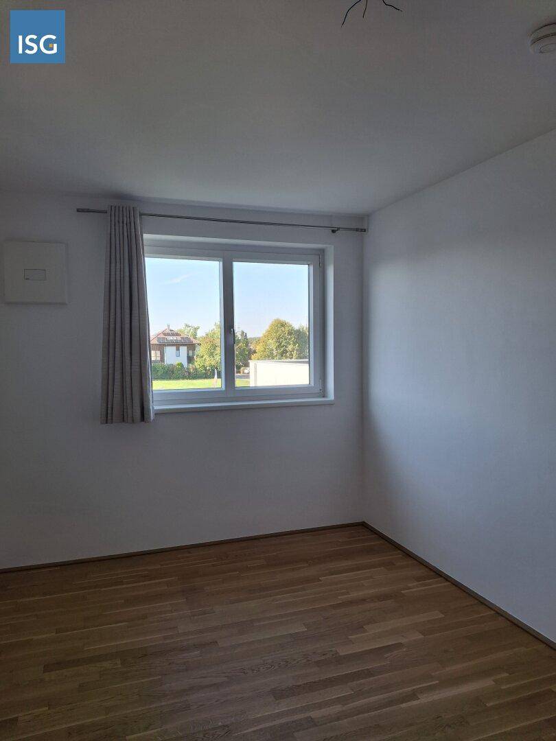Ruhiges, helles Schlafzimmer mit Parkettboden und einem Fenster mit Blick ins Grüne.